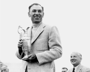 Ben Hogan smiling and holding the Claret Jug trophy after winning The Open Championship, wearing a light-colored textured jacket, with several men seated and standing in the background.