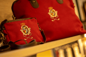 Close-up of red golf bags embroidered with the crest of Golf Club Villa d’Este, displayed on a wooden shelf in the pro shop.