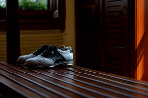 Pair of vintage black and white golf shoes resting on a wooden bench in the softly lit locker room.