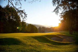 Sunset over the green at Golf Club Villa d’Este, with a bunker and flag in the foreground and forested hills in the distance.