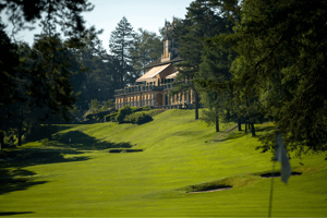 View of the Golf Club Villa d’Este clubhouse from the course, nestled in the hillside and surrounded by tall trees and manicured fairways.