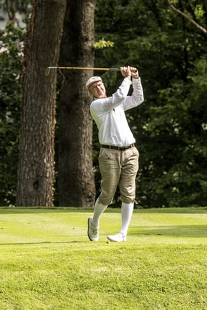 Golfer completing a follow-through with a vintage hickory golf club on a sunlit fairway.