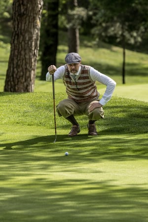 Golfer in traditional hickory golf clothing carefully reading the green before a putt during the Hickory Masters.