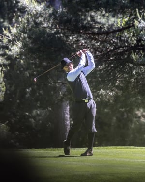 Golfer in vintage attire completing a swing with a hickory golf club on a tree-lined fairway during the Hickory Masters.