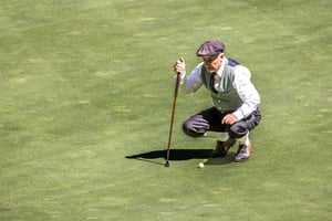 Golfer carefully reading the putting line while holding a vintage hickory putter on the green.