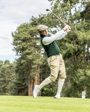 Golfer following through after a powerful tee shot with a vintage hickory golf club.