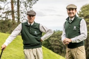 Two Hickory Masters participants wearing official event knitwear posing together on the golf course.