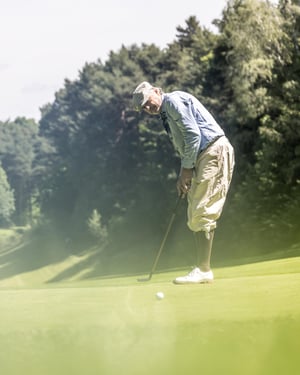 Hickory golfer practising a swing beside a vintage golf bag with classic wooden clubs in the foreground.