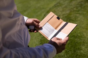 Close-up of a player holding a golf ball while checking the Hickory Masters scorecard between holes.