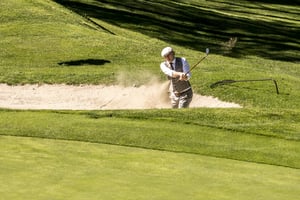 Golfer in vintage attire hitting a bunker shot with a hickory golf club during the Hickory Masters.