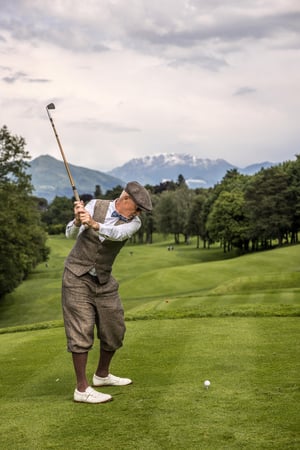 Hickory golfer at the top of the backswing on the tee with the Alpine landscape in the background.