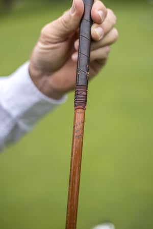 Close-up of a golfer holding a vintage hickory golf club with its original leather grip and wooden shaft.