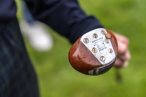 Close-up of a vintage hickory golf club with a wooden head and metal sole plate engraved with its original maker's markings.