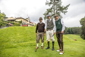 Three hickory golfers in traditional attire posing with their vintage clubs beside the Villa d’Este golf course.
