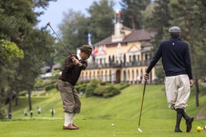 Hickory golfer preparing to strike the ball while another player watches beside the Villa d’Este clubhouse.