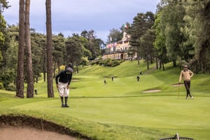Wide view of two hickory golfers on the green with the Villa d’Este clubhouse overlooking the fairway.