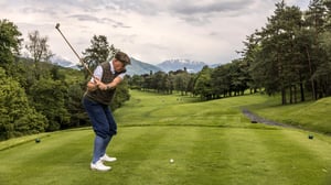 Golfer preparing to tee off with a hickory club overlooking the fairway and surrounding mountains.