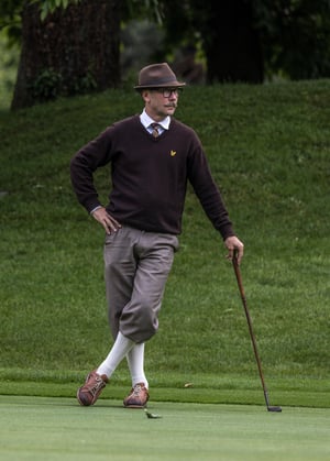 Hickory golfer leaning on a vintage putter while reading the green before a putt.