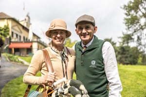 Two participants in vintage golf attire smiling together beside their hickory golf bags outside the Villa d’Este clubhouse.
