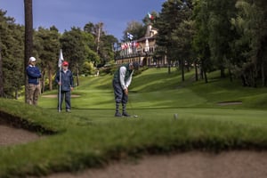 Hickory golfer putting on the green with the Villa d’Este clubhouse and spectators in the background.