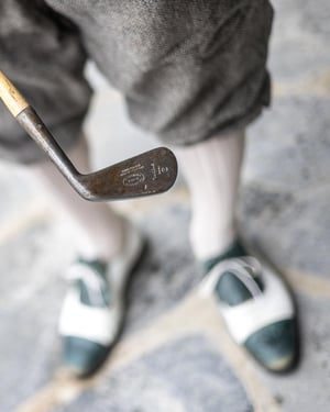 Close-up of the head of a vintage hickory golf club showing its forged markings and classic craftsmanship.