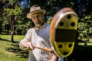 Close-up portrait of a hickory golfer presenting the face of a vintage wooden golf club toward the camera on the golf course.