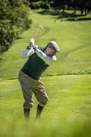 Golfer in classic hickory golf clothing completes a smooth follow-through with a vintage wooden club on a sunny golf course.