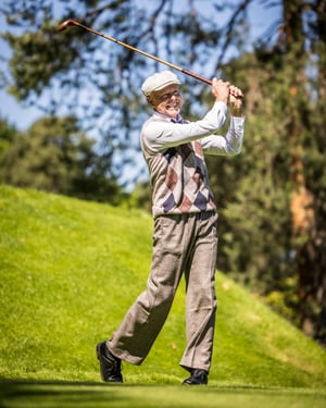 Close-up of a golfer in traditional hickory golf attire swinging a vintage iron on a scenic fairway during a practice round.