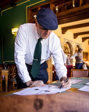 Golfer in traditional hickory golf attire signs the official players' booklet inside the clubhouse before the practice round.