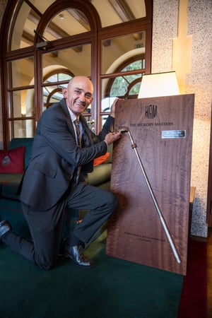 The winner of the first Hickory Masters in 2026 standing next to the wooden plaque featuring an original hickory bat, on which his name has been inscribed