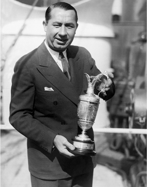 Golfer holding the Claret Jug trophy with both hands and smiling, dressed in a double-breasted suit, in a sunlit outdoor setting likely after winning The Open Championship