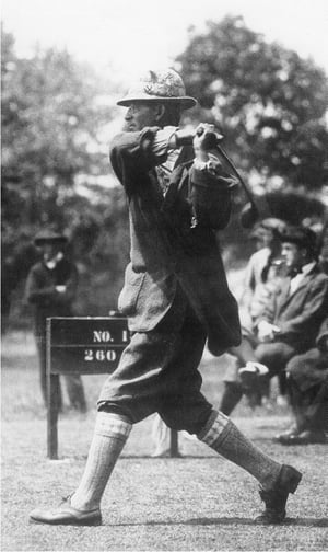 Vintage golfer captured mid-swing on the tee box, wearing traditional attire including plus fours, high socks, and a patterned hat, with a wooden club in hand and spectators in the background