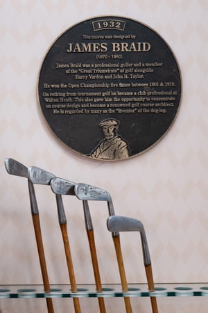 Commemorative plaque dedicated to James Braid displayed above a row of antique hickory-shaft irons.