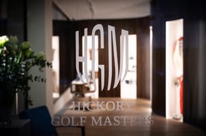 Close-up of the Hickory Golf Masters logo on a glass door, with softly illuminated museum displays visible in the background.
