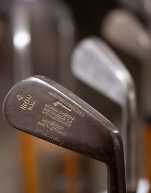 Bronze statue of a young caddie boy wearing a cap and suit, with a blurred museum visitor in the background.