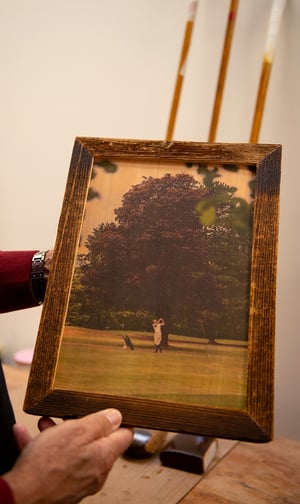 Vintage leather golf bag filled with antique wooden and iron golf clubs, displayed against a patterned wall.