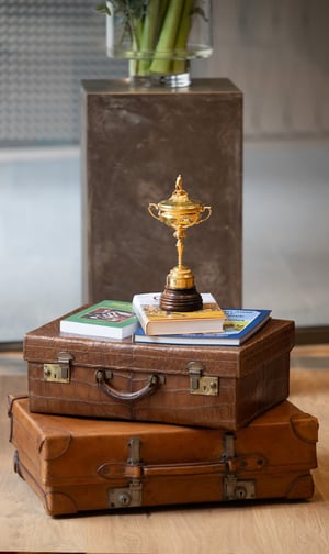 Hands holding a framed vintage golf photograph depicting a golfer playing under a large tree, with wooden clubs visible in the background.