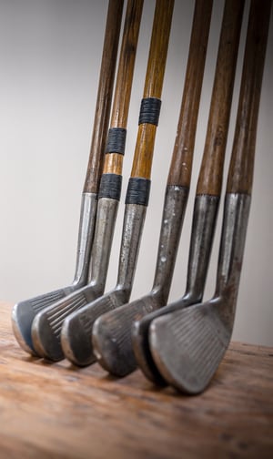 Two wall-mounted racks displaying a collection of antique hickory-shaft golf clubs with various grips and head styles.