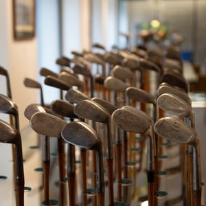 Large display of antique hickory-shaft golf irons arranged in dense rows, showcasing aged steel clubheads and wooden shafts inside the museum.
