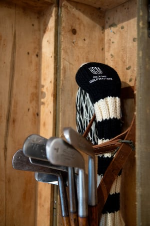 Vintage golf clubs stored inside an old wooden travel case, with a knitted black-and-white Hickory Golf Masters club cover.